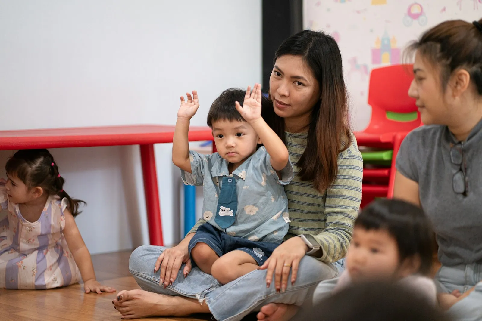 A teacher sitting with a group of happy toddlers in a classroom