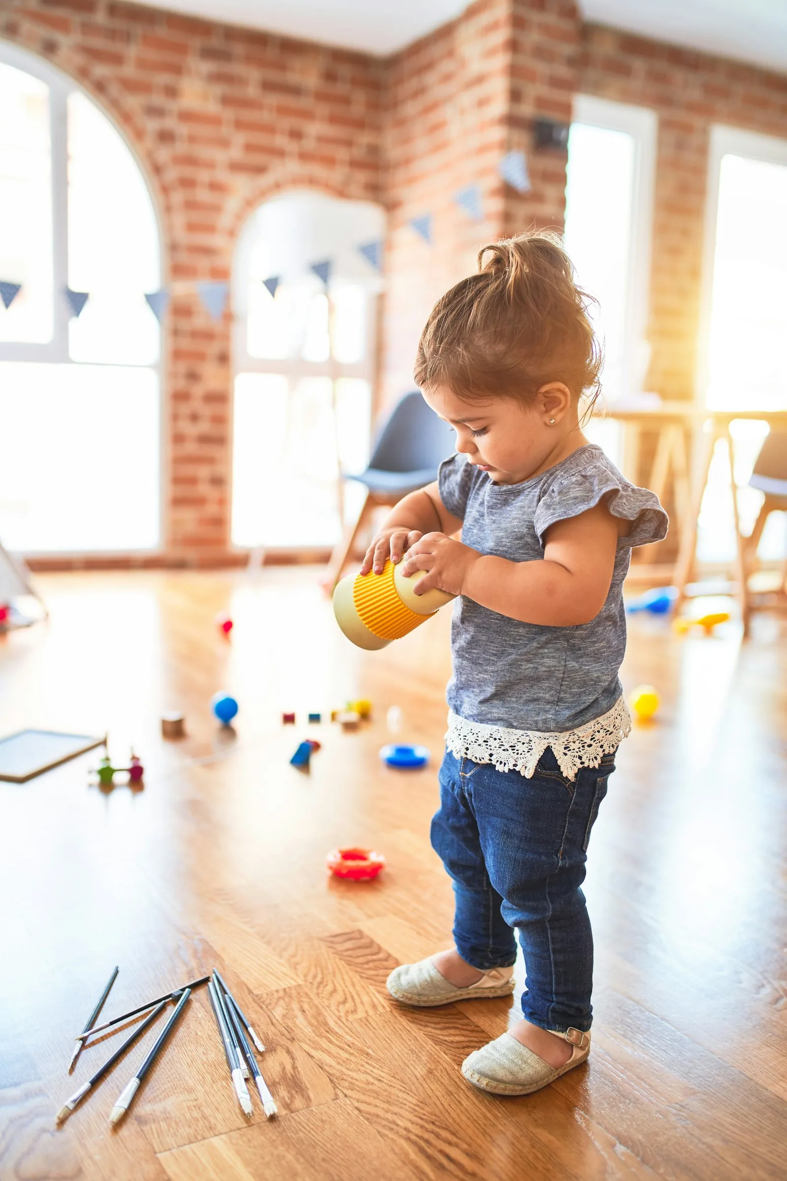 A toddler playing with a cup in a bright playroom